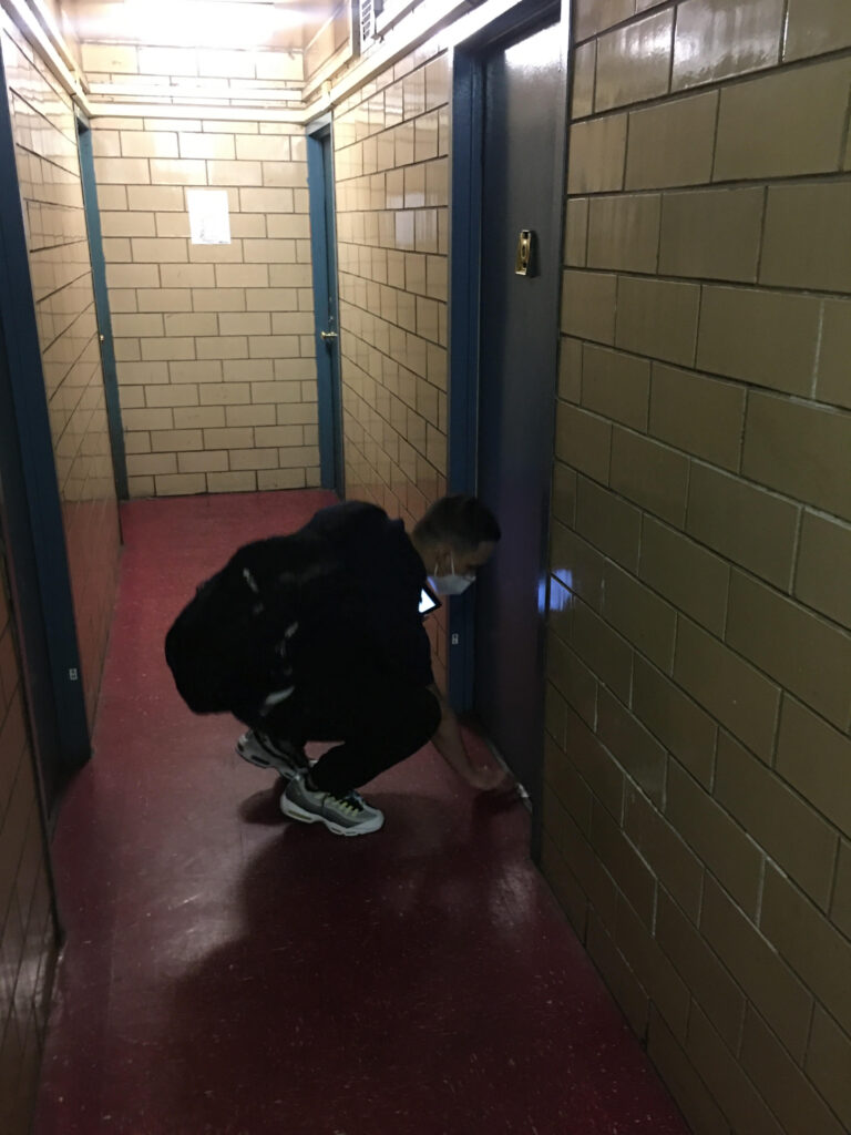 man sliding a paper beneath the door of a NYCHA apartment