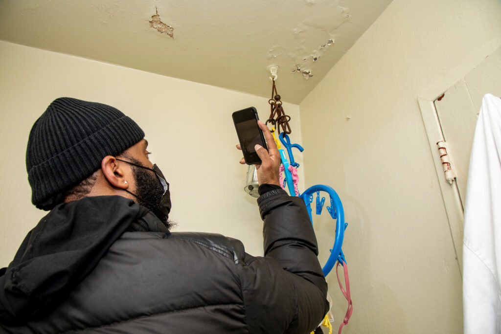 man holds smartphone up to take a photo of peeling paint on a ceiling