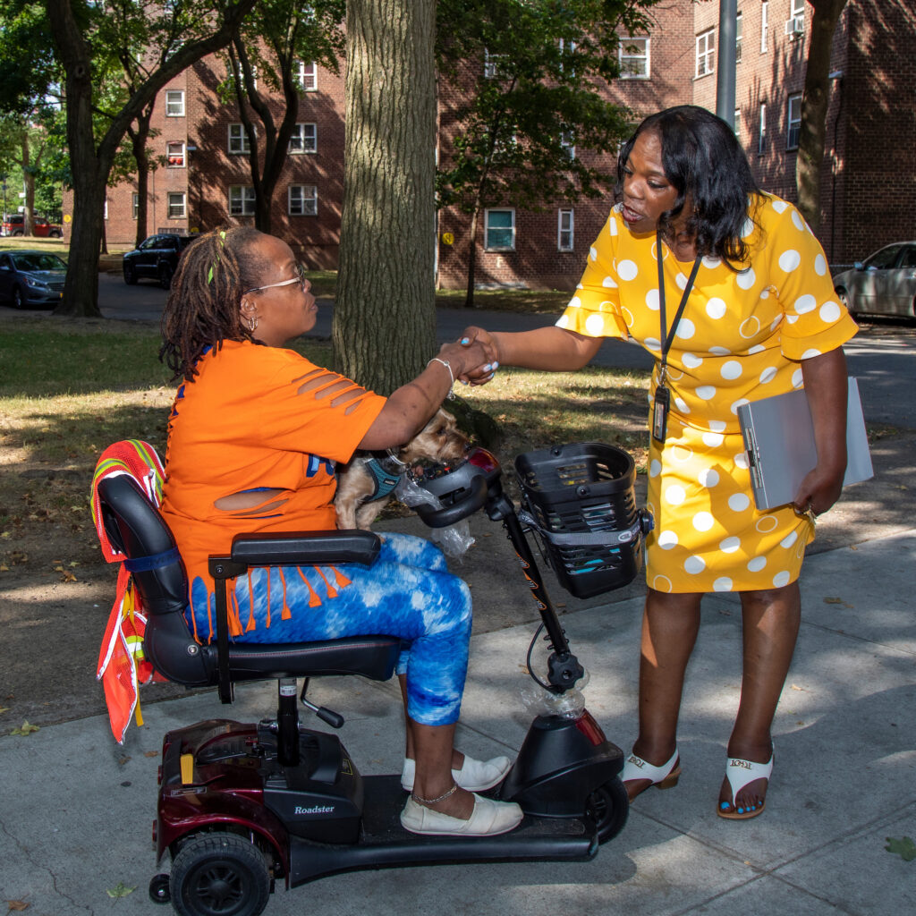 woman in yellow dress shakes hand with woman in an orange shirt and wheelchair