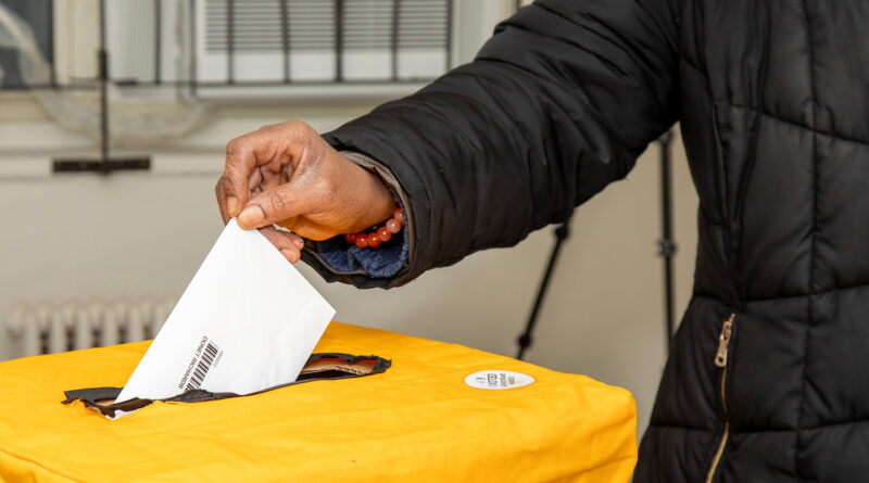hand of a person inserting a ballot into a ballot box