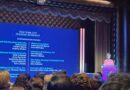 woman at podium with large screen on stage