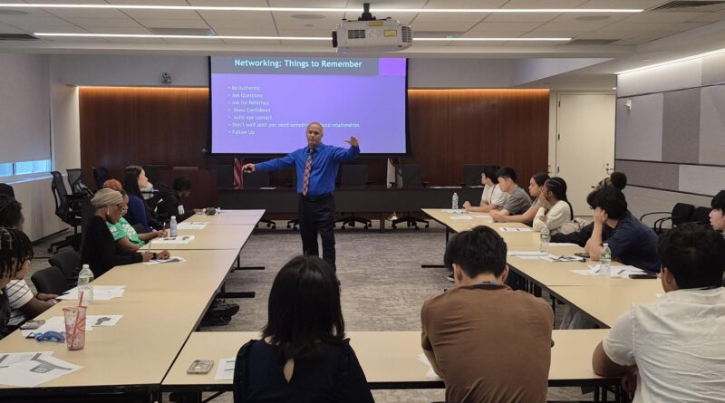man standing in middle of room talking to people in seats