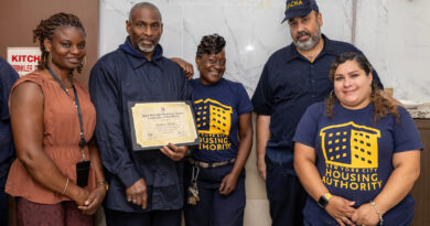 A group of five individuals, including one holding a certificate, stand together in a room with a “New York City Housing Authority” logo on their shirts.