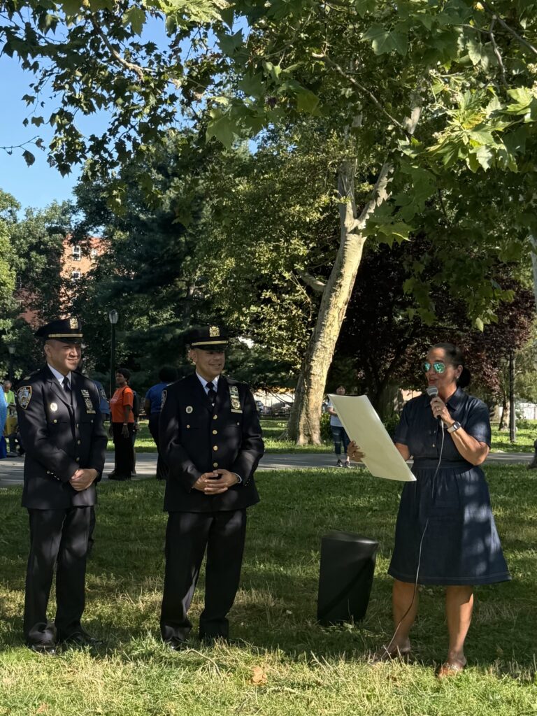 woman holding a large paper standing next to two officers in uniform