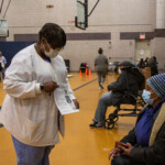 COVID-19 Vaccine Distribution at Van Dyke Houses Community Center. masked woman showing another masked woman a paper